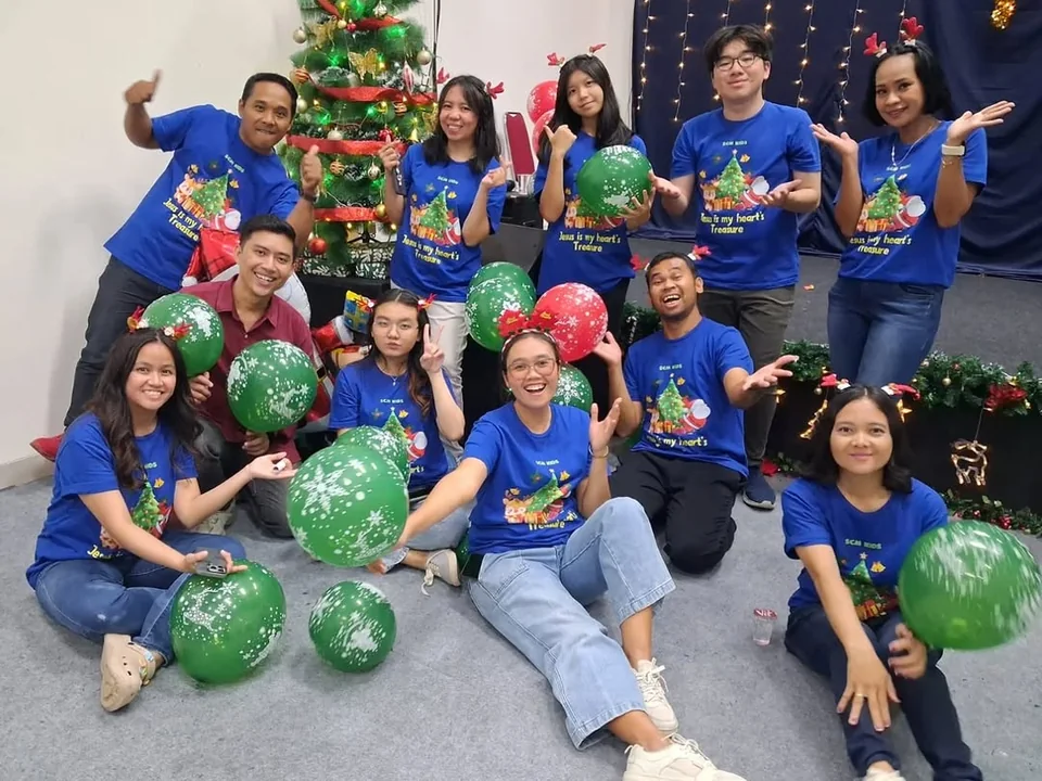 Kakak-kakak Sekolah Minggu GBI SCM berfoto bersama dengan kaus biru dan dekorasi Natal.